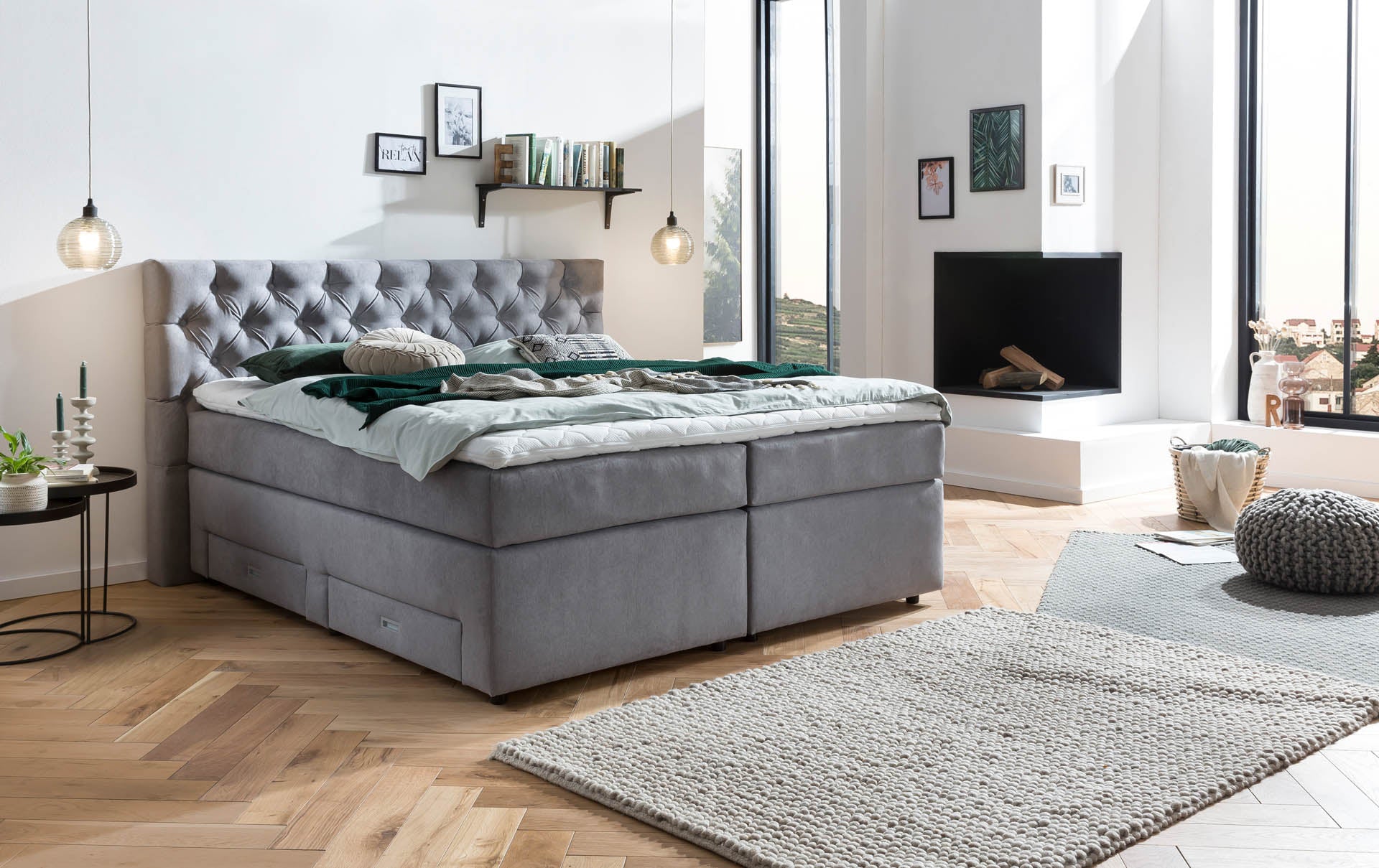 Gepolstertes Kopfteil eines Boxspringbettes in Dunkelgrau mit tiefer Knopfheftung mit weißem Topper und Zierkissen