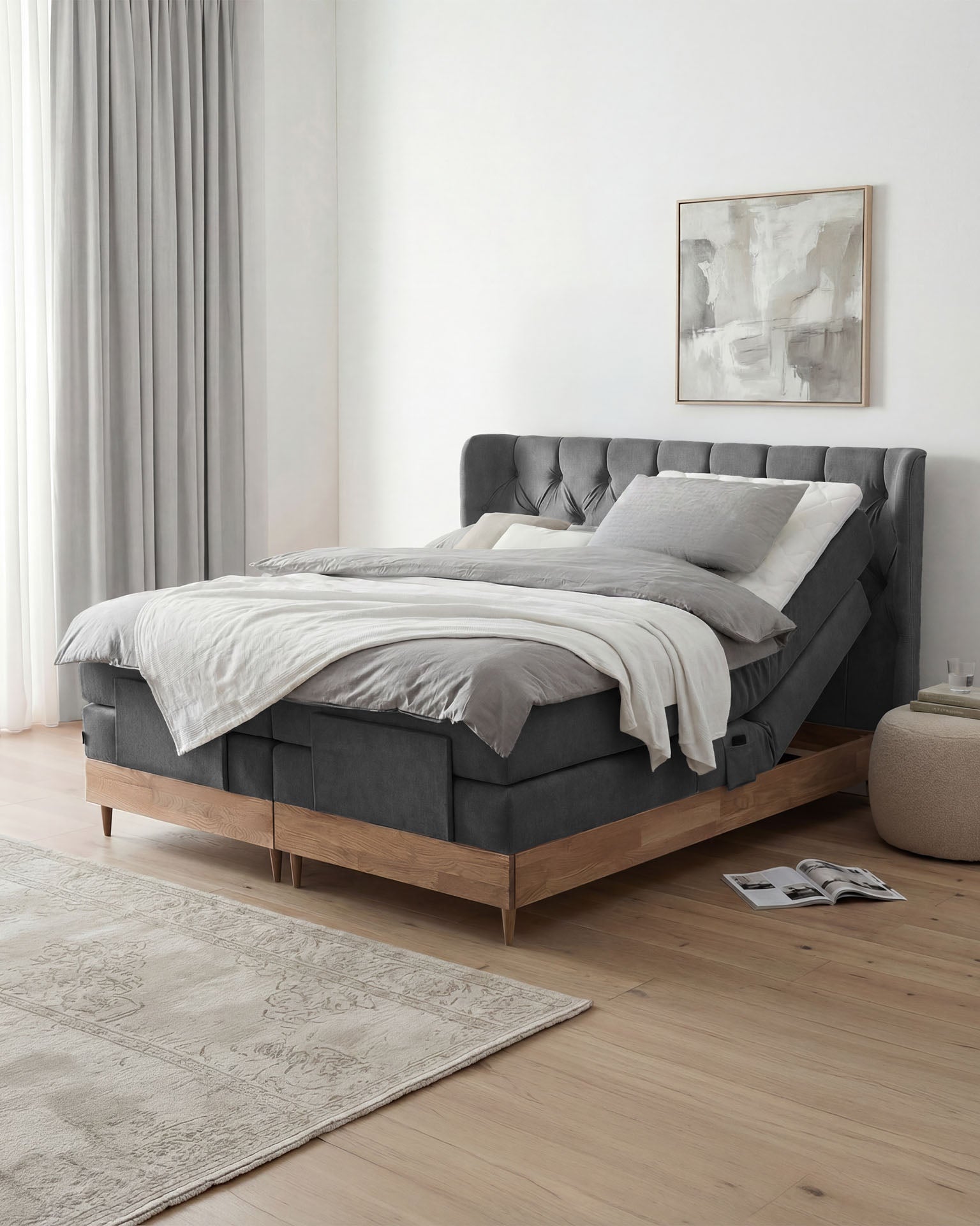 Graues Polsterbett mit gestepptem Kopfteil, hellem Holzrahmen und weiß-grauer Bettwäsche in einem modernen Schlafzimmer