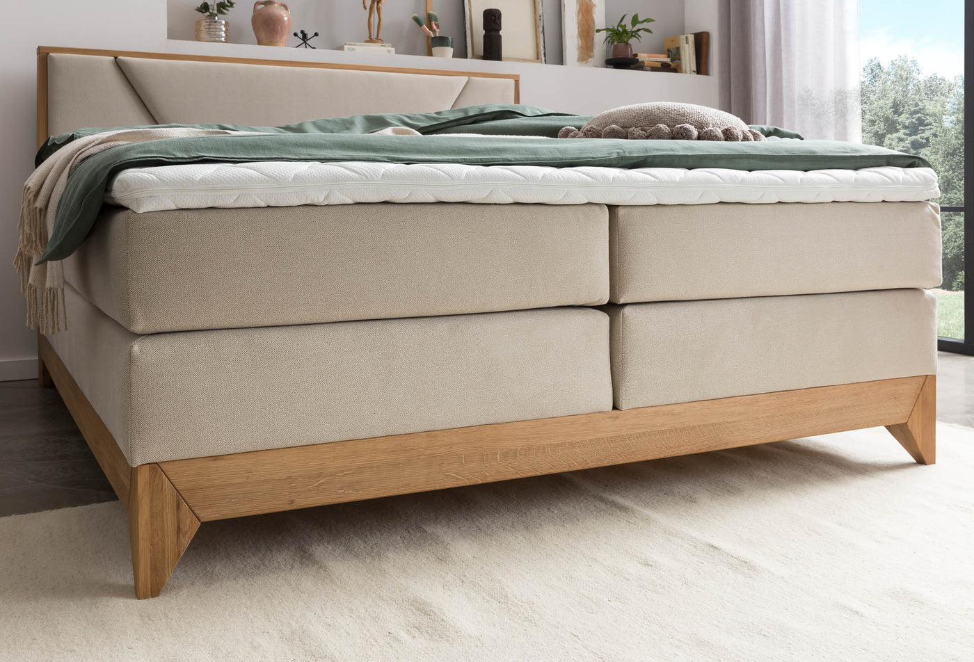 Detailansicht eines Boxspringbetts in Beige mit dreilagigem Aufbau (Box, Matratze, Topper) und Holzuntergestell mit Füßen.